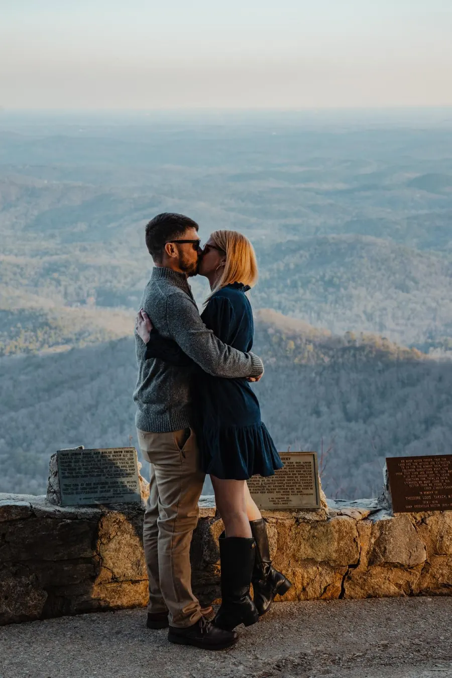 A couple kissing at a stone overlook with Blue Ridge ridgelines fading out behind them